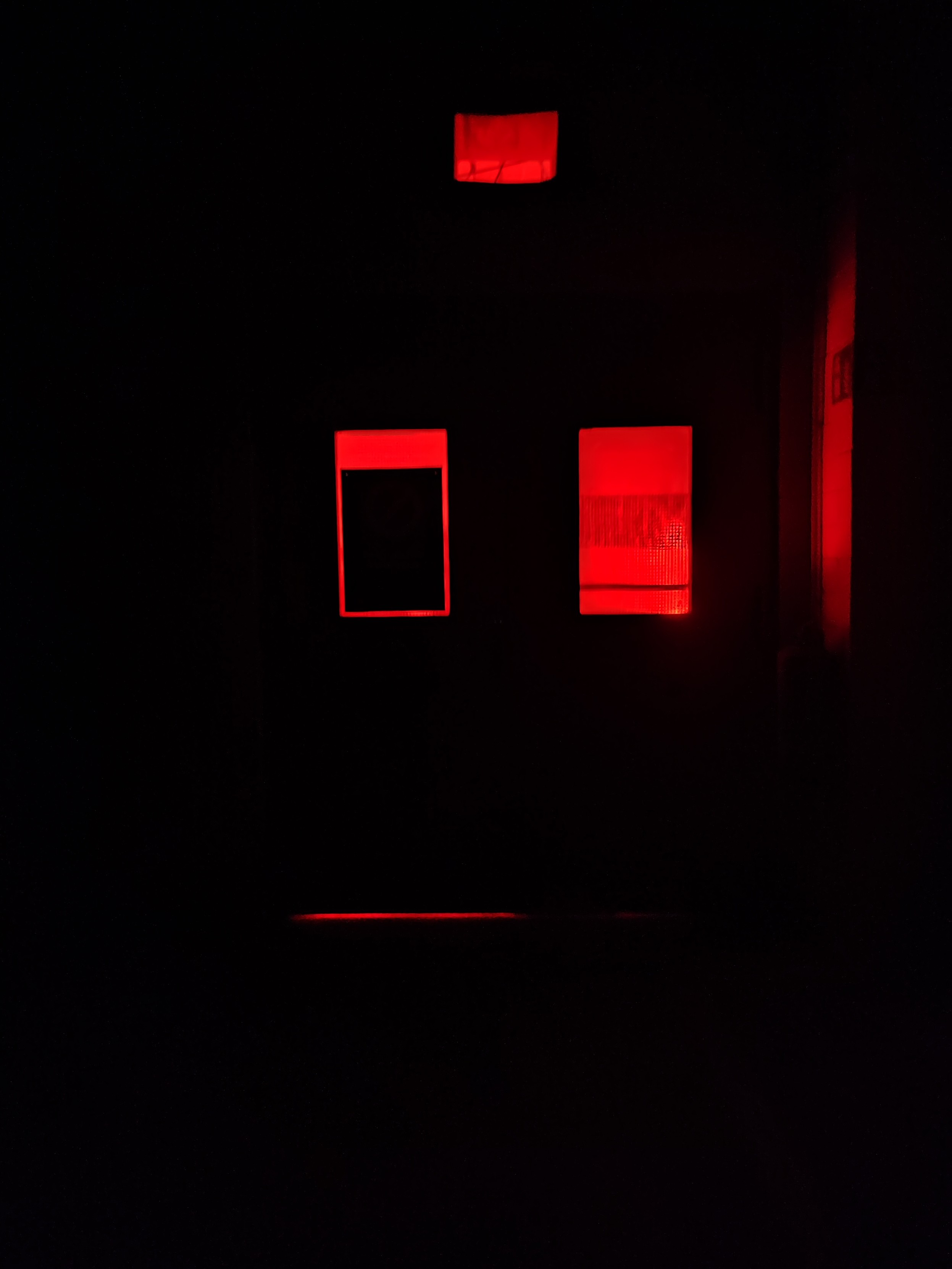 Eine Doppeltür in einer funklen Hslle, durch dir Fenster scheint rotes Licht.